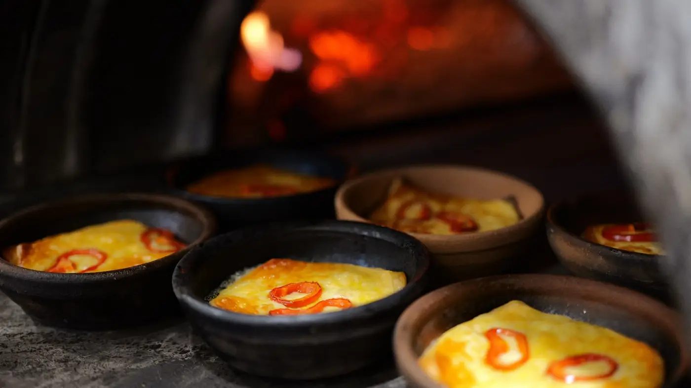 Clay pots of baked cheese with peppers in front of the wood-fired oven