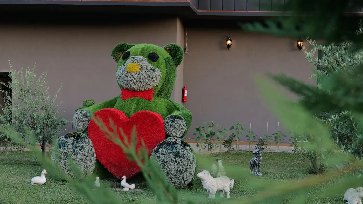 Large green topiary bear holding a red heart in the garden