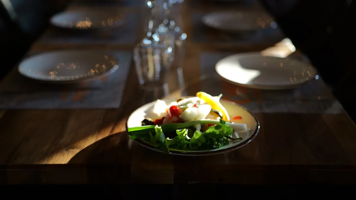 Village salad on a sunlit wooden table set with plates and glasses