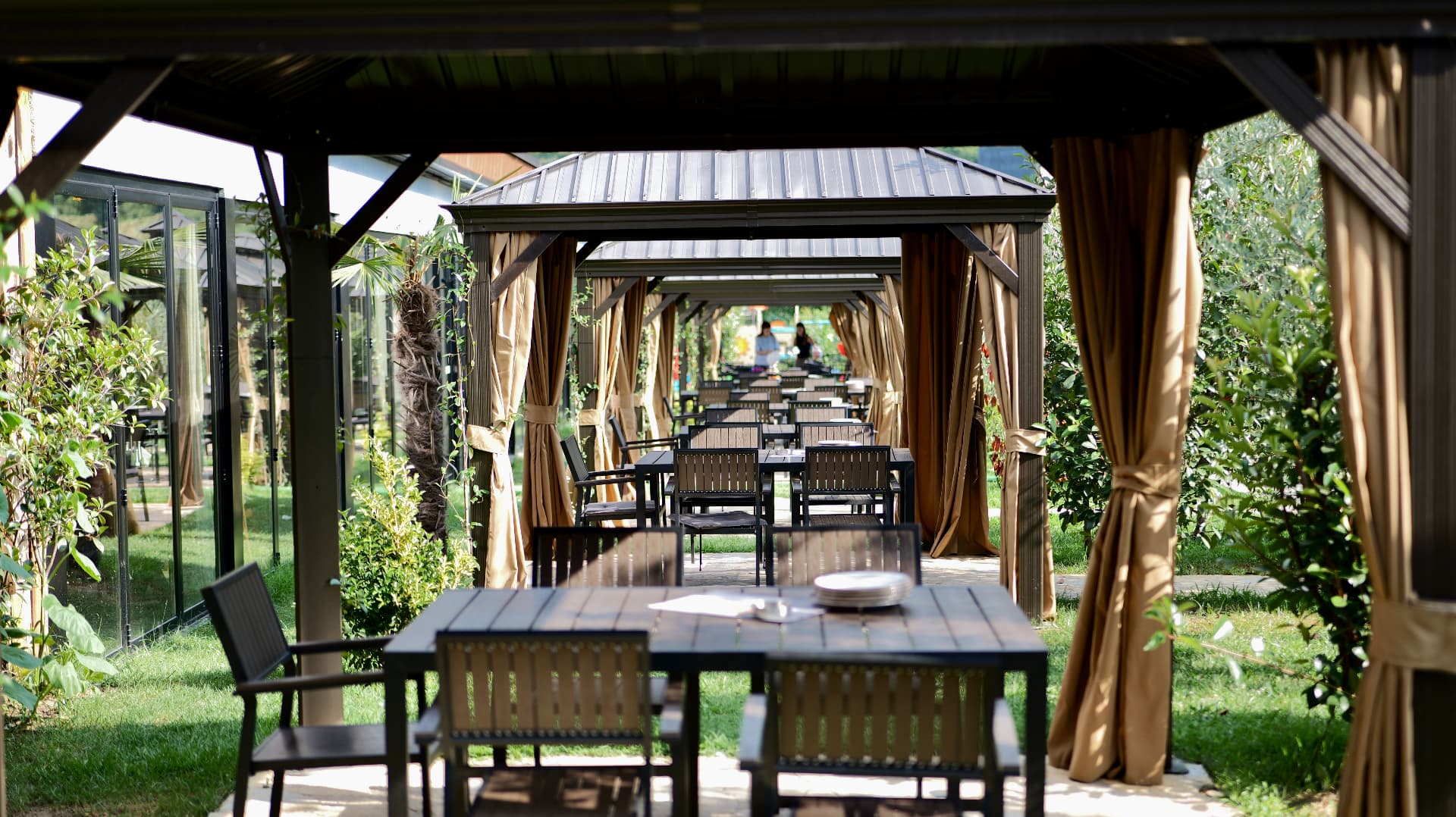 Covered gazebos with curtains and set tables in the green garden of OKO Farm