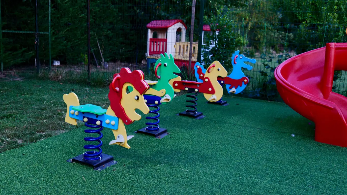 Children's playground with spring riders and a red slide on the lawn at OKO Farm
