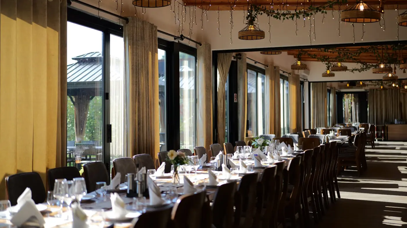 Long indoor dining hall at OKO Farm set for a large group, with warm string lights